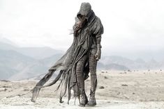 a woman dressed in grey walking across a desert