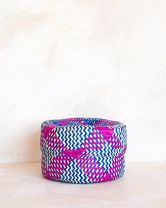 a pink and blue basket sitting on top of a white table next to a wall