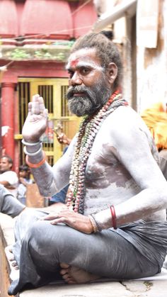 a man with white paint on his face and beard sitting in front of a building