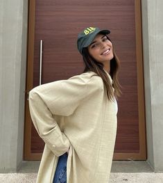 a woman standing in front of a brown door wearing a hat and coat with the word big written on it