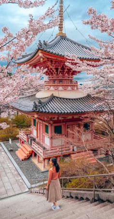 a woman standing in front of a tall building with cherry blossoms on the trees around her