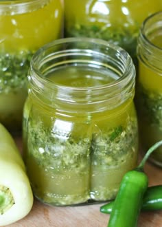 several jars filled with pickles and vegetables on top of a wooden table next to green peppers