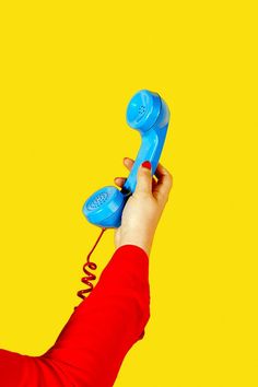 a person holding an old fashioned blue phone in their hand against a bright yellow background