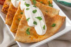 three quesadillas on a plate with sour cream and tomatoes in the background