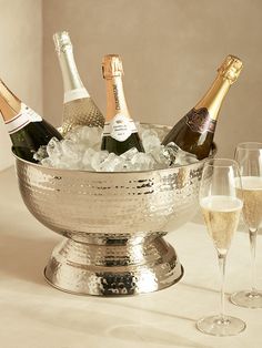 several bottles of champagne in a silver ice bucket with two glasses on the table next to it