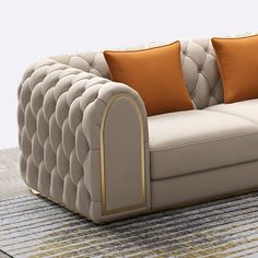 a couch with two orange pillows on top of it and a rug underneath the couch