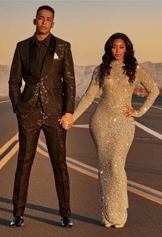 a man and woman in formal wear standing on the side of an empty road holding hands