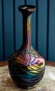 a colorful glass vase sitting on top of a wooden table next to a blue wall