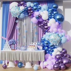 a table topped with balloons next to a purple and blue wall covered in snowflakes