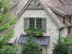 an old brick house with green shutters and flowers in the window box on the roof