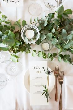 the table is set with silverware and greenery for an elegant touch to the place setting