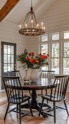 a dining room table with four chairs and a vase on the table in front of it