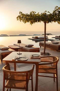 an outdoor dining area with tables and chairs overlooking the water at sunset or sunrise,