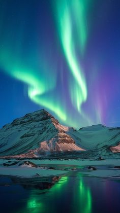 the northern lights shine brightly over mountains and snow covered ground, reflecting in still water