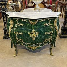 an ornate green and gold chest with marble top on display in a furniture showroom