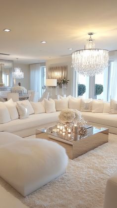 a living room filled with white furniture and chandelier hanging from the ceiling,