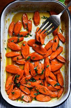 carrots are being cooked in a casserole dish with a fork and parsley