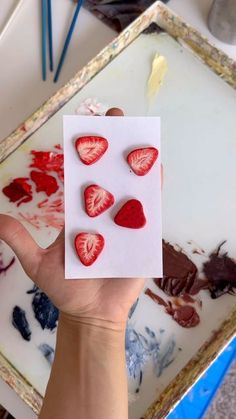 someone is holding up some strawberries on a piece of paper with paint splattered all over them