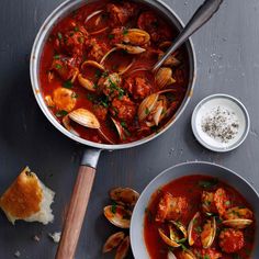 two bowls of stew with clams and bread next to it on a gray surface