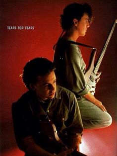 two young men sitting next to each other holding guitars