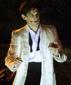 a man in a white jacket and black tie holding his hands out to the side