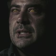 a close up of a man with yellow eyes looking at something in the dark,