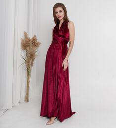 a woman in a long red dress standing next to a vase with flowers on it