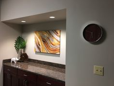 a large clock mounted to the side of a wall next to a counter top with a vase on it