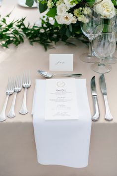 the table is set with silverware and white flowers