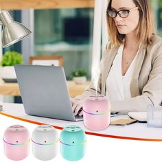 a woman sitting in front of a laptop computer on top of a white table next to three small bluetooth speakers