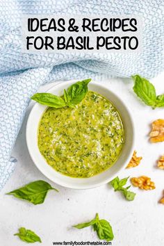 a white bowl filled with pesto sauce surrounded by leaves and walnuts on a blue towel