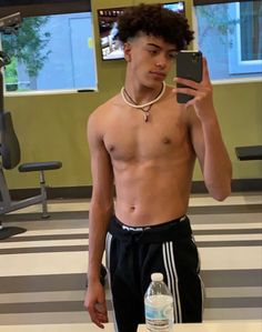 a shirtless young man taking a selfie with his cell phone in the gym