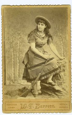 an old time photo of a woman with a hat and dress sitting on a log