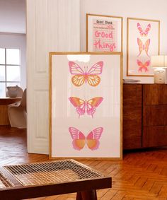 three framed pictures with pink and orange butterflies on them in front of a wooden table