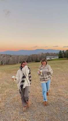 two women walking in a field at sunset, one holding a cup and the other carrying a frisbee