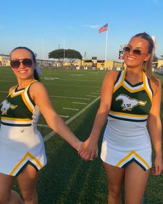 two cheerleaders are holding hands on the field