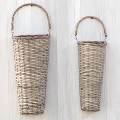 two wicker baskets hanging on the side of a white wooden wall, one holding a handle