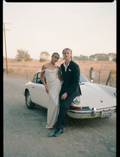 a man and woman standing next to a white car