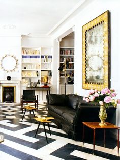 a black and white checkered floor in a living room with two couches, coffee table, bookshelf and fireplace