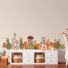 a toy giraffe standing next to a white table with baskets on it and houses painted on the wall