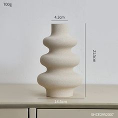 a tall white vase sitting on top of a wooden table next to a filing cabinet