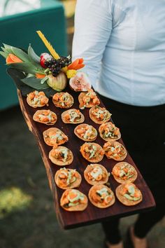 a person holding a wooden tray with small food items on it in front of them