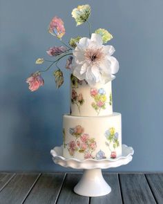 a three tiered cake decorated with flowers on a table next to a blue wall