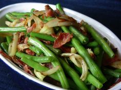 a white bowl filled with green beans and bacon on top of a blue table cloth