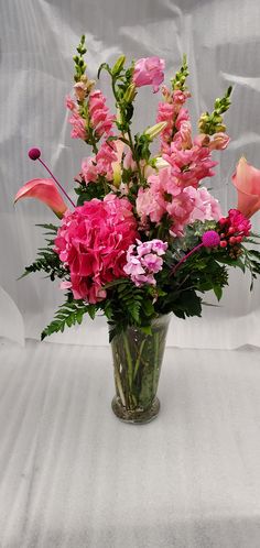 a vase filled with lots of pink flowers on top of a white cloth covered table