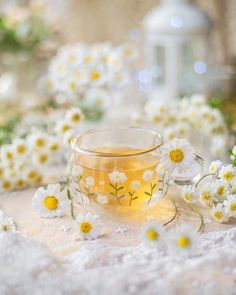 a glass cup filled with tea surrounded by daisies and small white flowers on a table