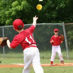 two young boys playing baseball on a field with one throwing the ball to the other