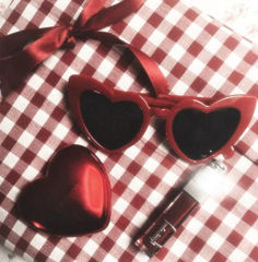 two heart shaped sunglasses on top of a red and white checkered table cloth next to a bottle of perfume