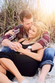 a man and woman sitting in the sand together, holding each other's hands