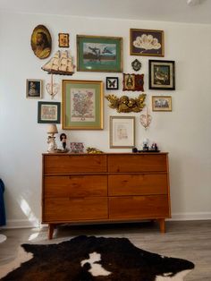 a dresser with many pictures on the wall above it and a cow hide rug underneath